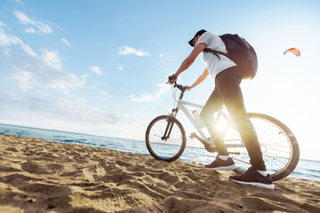 male tourist with a bicycle walking along a sandy beach .