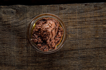 Patè di olive in una ciotola di vetro isolata su sfondo legno