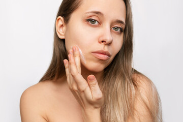Fototapeta premium Portrait of a young beautiful caucasian blonde woman with makeup touching the face with her hand applying a moisturizing cream on the skin isolated on a white background. Beauty and fashion. Skin care