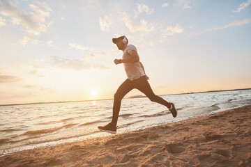 sporty man running fast on a sandy beach at sunset.