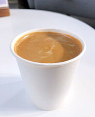 Espresso with milk and tiger foam in a disposable paper cup on a white table - 492058161