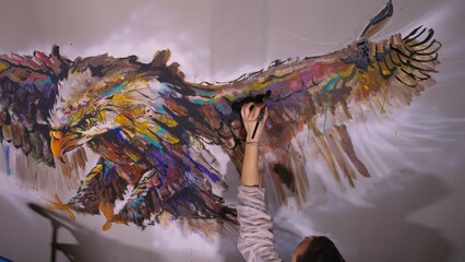 Artist designer draws an eagle on the wall. Craftsman decorator paints a picture with acrylic oil color. Painter painter dressed in a paint coat. Indoor. Dark magic cinematic look.