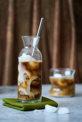 Cold coffee with ice and milk. Cold coffee in a glass cup on a green napkin. Cold coffee with a metal straw.