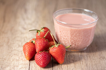 Strawberry flavored milk in clear glass on wooden background