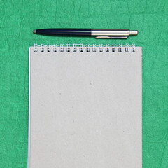 White and gray notepad sheet with spiral with pen against the background of green fabric. Concept of analysis, study, attentive work. Stock photo with empty place for your text and design. Square