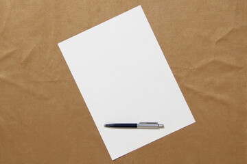 Template of white paper with pen lies diagonally on light brown cloth background. Concept of...