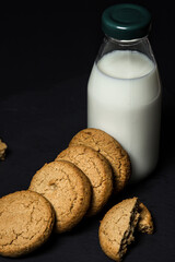 Oatmeal cookies with a bottle of milk on a black background. Light and tasty dessert. Healthy breakfast