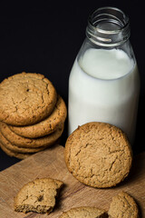 Oatmeal cookies with a bottle of milk on a black background. Light and tasty dessert. Healthy breakfast