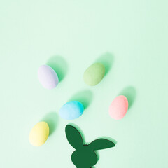Fototapeta na wymiar Rabbit is thinking about Easter Holiday with colorful eggs above his head on pastel green background with copy space for text. Minimal Easter concept with bunny and colored egg for upcoming season.