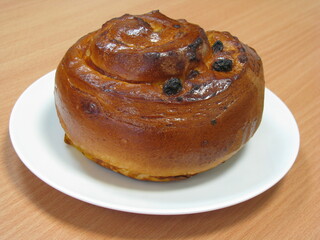 Bun with cream and raisins. A bun on a white plate stands on the table.