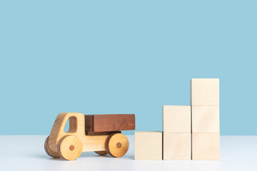 A wooden toy car stands next to a pyramid ladder made of wooden cubes on a blue background. The concept of logistics and cargo transportation.