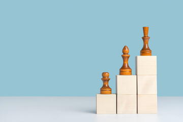 Black chess pieces stand on wooden cubes arranged in the form of a ladder up. The concept of growth...