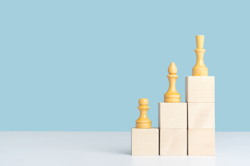 Wooden cubes arranged in the form of stairs and pyramids, on which chess pieces are arranged in order of importance, pawn-officer and queen. Layout for a business concept