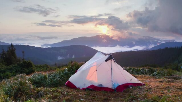 Morning dawn after rain with fog on the alpine stone wastelands of the Montenegrin ridge and Hoverla of the Carpathians of Eastern Europe. White tent glows in the rays of dawn over a misty valley