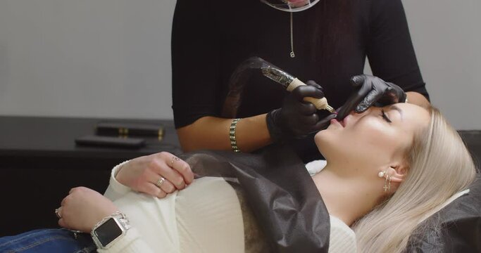 Permanent makeup. The master makes a lip tattoo for a client in a beauty salon.