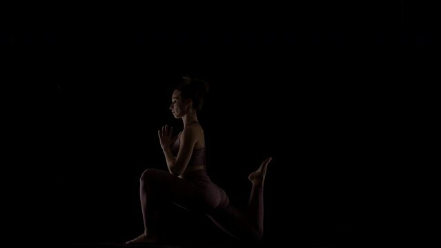 Fit woman practicing yoga poses. Silhouette girl doing exercise indoors against black background. No stress inner balance concept..