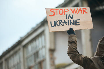 Close-up of demonstrator walks with 'stop war in Ukraine' placard among ruined city streets.