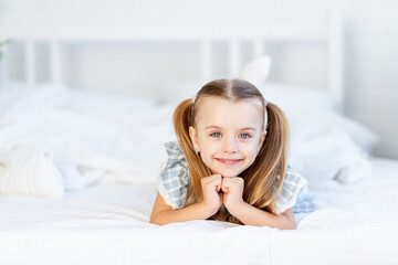a girl child on the bed at home on a white cotton bed lies and smiles sweetly