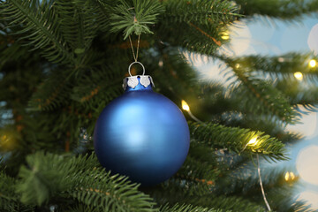 Obraz na płótnie Canvas Beautiful blue bauble hanging on Christmas tree against blurred festive lights, closeup