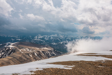 Awesome top view through clouds to high snowy mountains. Scenic landscape with beautiful snow mountains in low clouds. Atmospheric alpine view from stone hill to snow mountain range with low clouds.