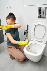 woman covering nose to avoid bad smell while cleaning a smelly toilet bowl