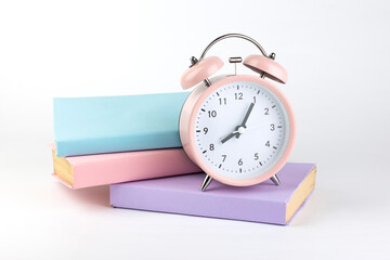 Pink  alarm clock and colorful books on white  isolated background.Education concept.