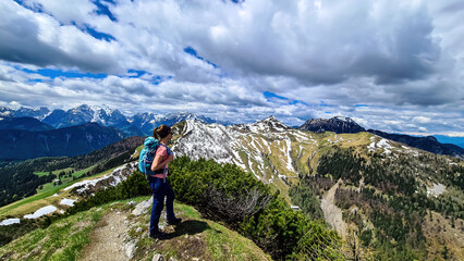 Fototapeta premium Hiker woman with backpack at summit of Hahnkogel (Klek) with scenic view on mountain peaks in Karawanks and Julian Alps, Carinthia, Austria. Border with Slovenia. Triglav National Park. Goal seeking