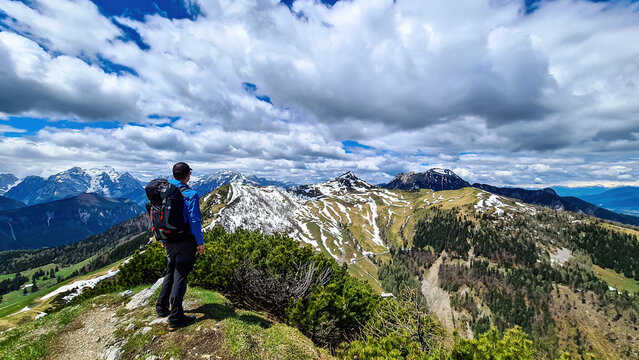 Hiker man with backpack at the summit of Hahnkogel (Klek) with scenic view on mountain peaks in the Karawanks and Julian Alps, Carinthia, Austria. Border with Slovenia. Triglav National Park