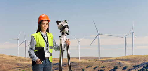 Young female geodetic surveyor with a measuring equipment on wind turbine farm