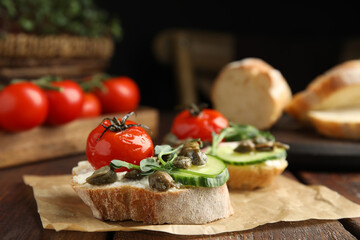 Tasty bruschettas with vegetables and capers served on wooden table, closeup