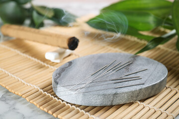 Grey stone coaster with acupuncture needles on bamboo mat - obrazy, fototapety, plakaty