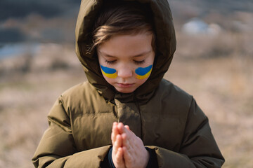 Ukrainian boy closed her eyes and praying to stop the war in Ukraine. Hands folded in prayer concept for faith, spirituality and religion. War of Russia against Ukraine. Stop War