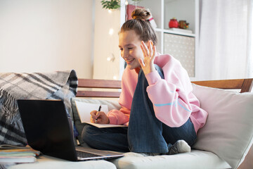 Millennial teen girl sit at couch in living room study on laptop making notes