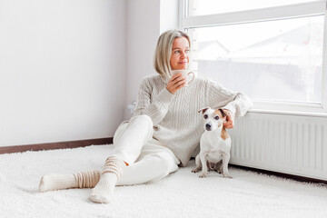 Happy woman in a cozy sweater with dog at home next to the radiator
