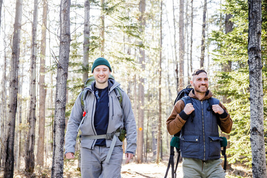 Male Friends With Backpacks Hiking In Snowy Woods