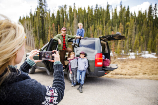 Mother with camera phone photographing family outside car at roadside