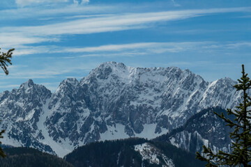Fototapeta premium Scenic view of snow capped mountain peaks of Karawanks on the way to Sinacher Gupf in Carinthia, Austria. Mount Wertatscha is visible through dense forest in early spring. Rosental on a sunny day.Hike