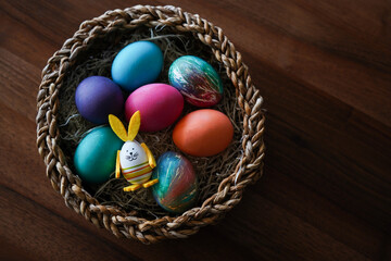 colourful Easter eggs in the nest with cute bunny shaped easter ornament on wooden table