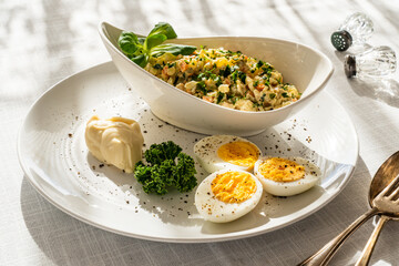 Vegetable mayonnaise salad with hard boiled eggs on white table
