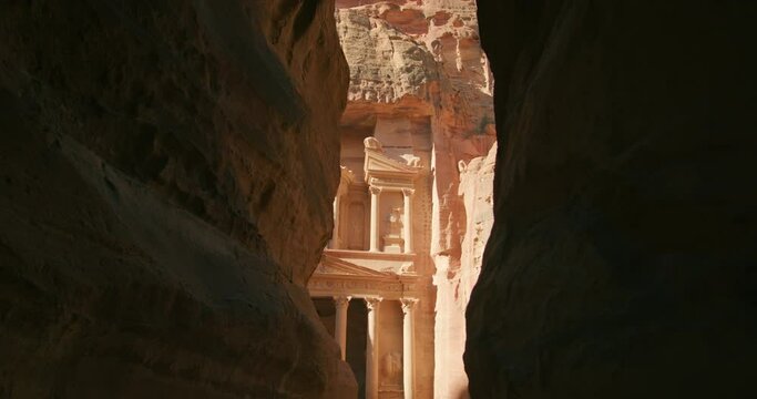 The Siq gorge opens to Petra's temple - Treasury Al-Khazneh. Temples carved out of sandstone rock face in Nabatean city inhabited by Arabs in ancient times. Most popular tourist attraction in Jordan.