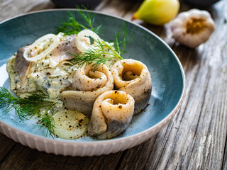 Swedish style marinated herring fillets in mayonnaise and cream with pickled cucumber, parsley, onion, garlic and dill on wooden table
