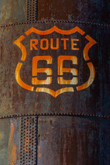 Weathered stained Route 66 emblem marker on the side of a large very rusty tank on Route 66 in Arizona.
