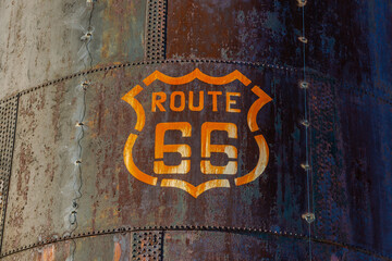 Weathered stained Route 66 emblem marker on the side of a large very rusty tank on Route 66 in...