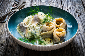 Swedish style marinated herring fillets in mayonnaise and cream with pickled cucumber, parsley, onion, garlic and dill on wooden table

