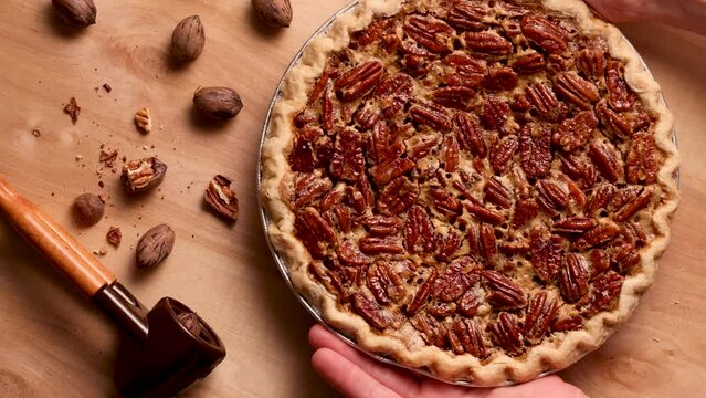 Hands place home made pecan pie on rustic wooden table, top view. This is the official dessert of Texas State.
