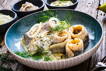 Swedish style marinated herring fillets in mayonnaise and cream with pickled cucumber, parsley, onion, garlic and dill on wooden table
