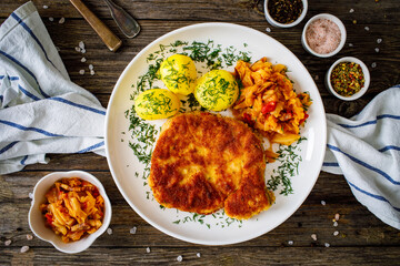 Breaded fried pork chop with boiled potatoes and cabbage on wooden table

