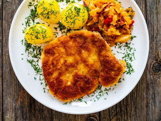 Breaded fried pork chop with boiled potatoes and cabbage on wooden table
