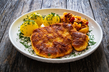Breaded fried pork chop with boiled potatoes and cabbage on wooden table
