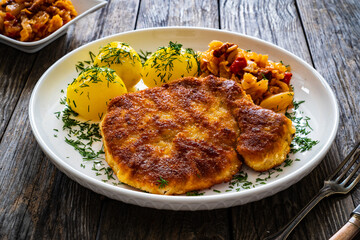 Breaded fried pork chop with boiled potatoes and cabbage on wooden table
